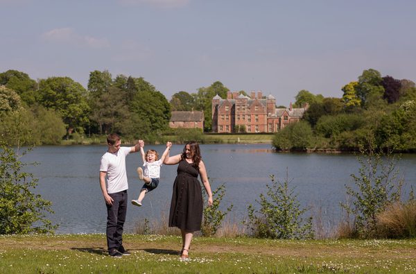 Family swinging child and walking next to lake with Kiplin Hall in background